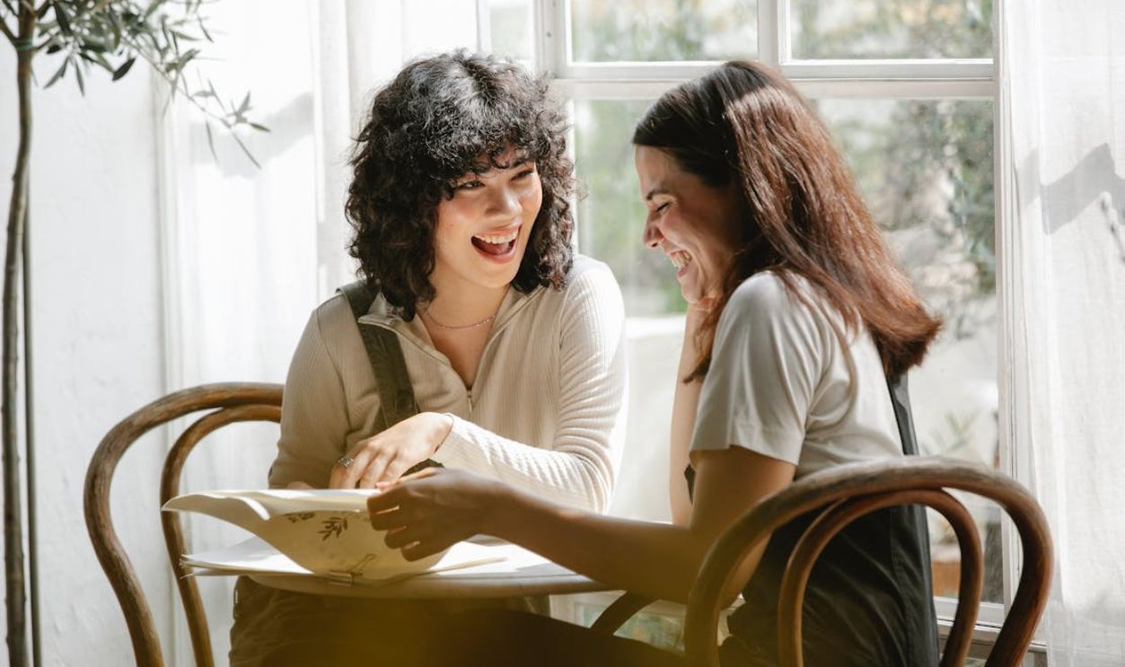 Cheerful diverse girlfriends reading document at table