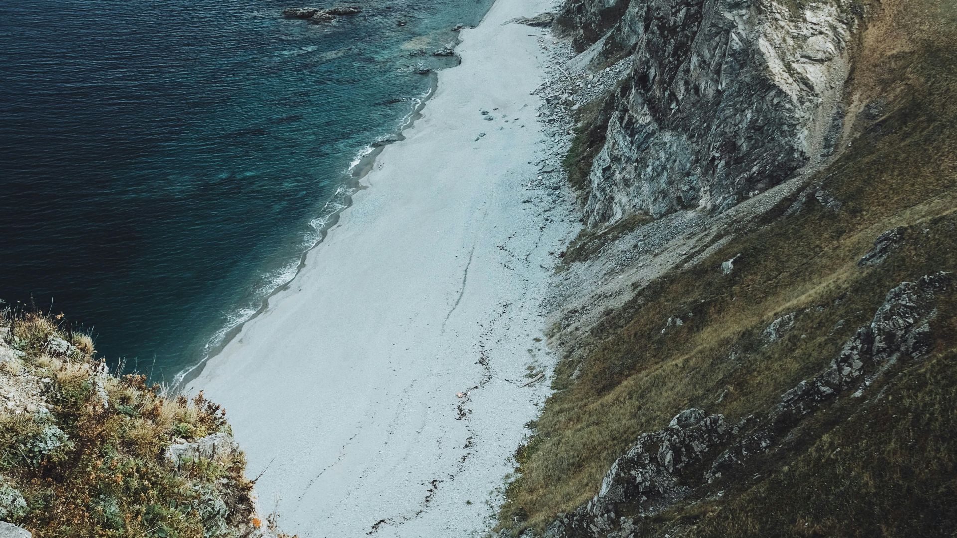 Breathtaking view of rugged cliffs and sandy shoreline meeting the ocean under a clear sky.