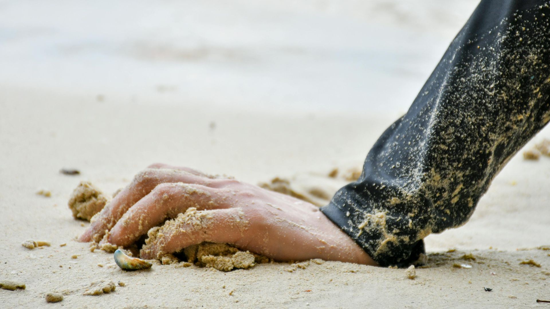 Close-up of a hand resting on sandy beach, capturing the serene and peaceful beach ambiance.