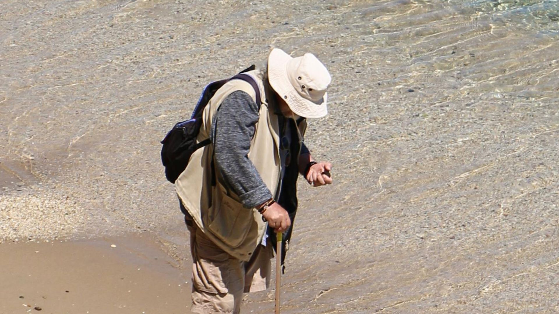 A senior man with a hat and walking stick explores a scenic beach coastline.