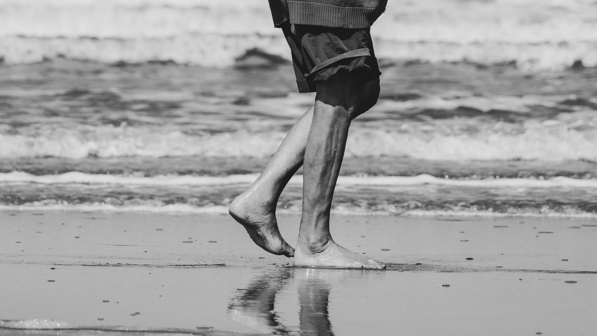Black and white photo of an elderly man strolling on a peaceful beach in summer.