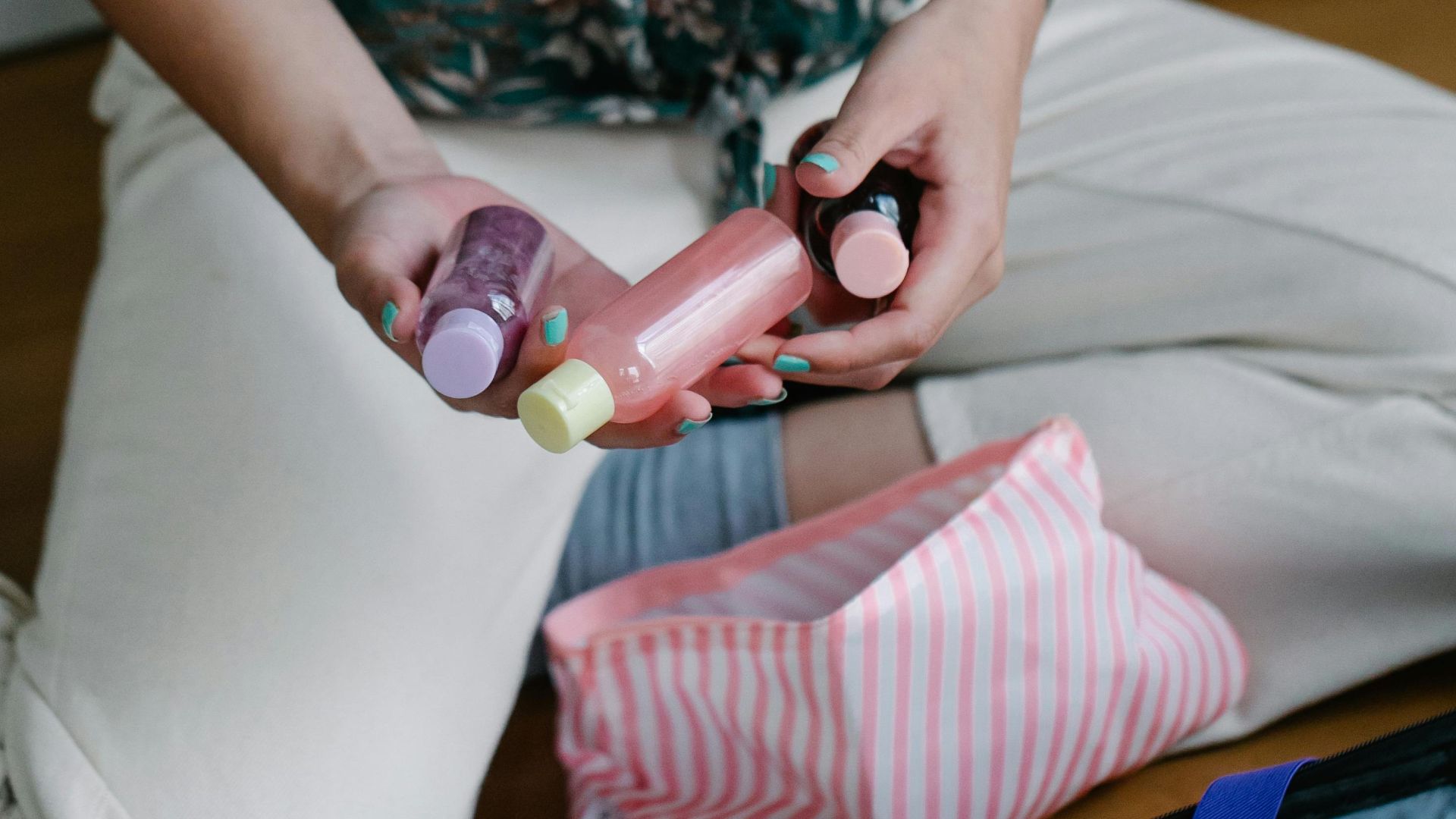 Person organizing toiletries in suitcase for a trip, featuring travel-size bottles and a striped pouch.