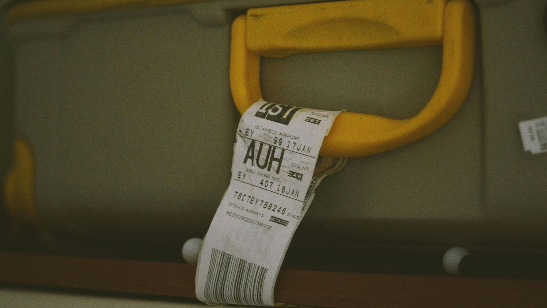 Close-up of a yellow suitcase handle with a visible travel tag and barcode, ideal for travel themes.
