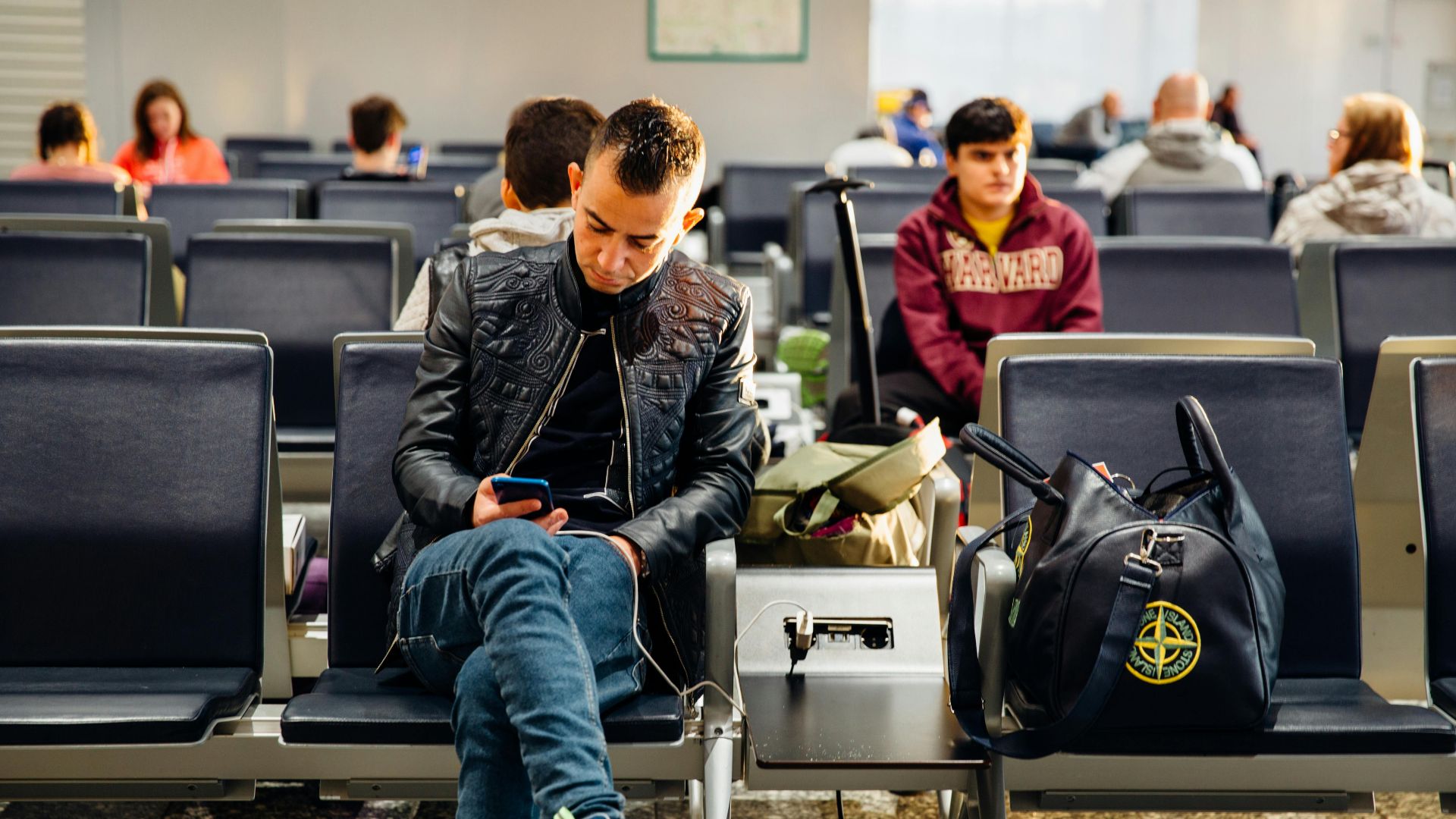People sitting in an airport lounge, focused on smartphones and waiting for flights.