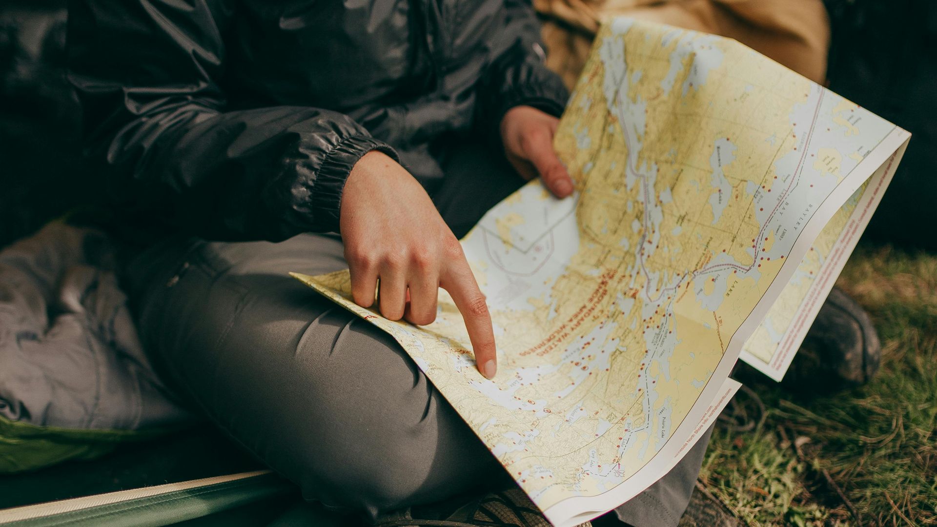 A woman sits in a tent studying a map during a camping trip in the wilderness.