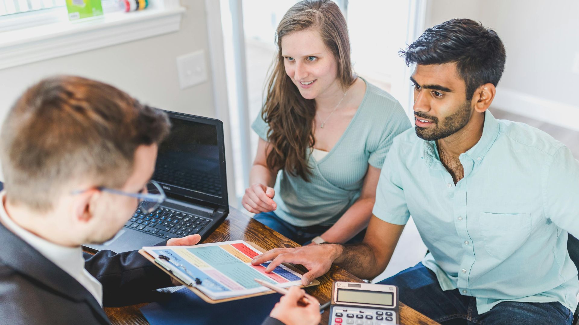 A couple consults with a real estate agent about buying a new home, papers and calculator on the table.