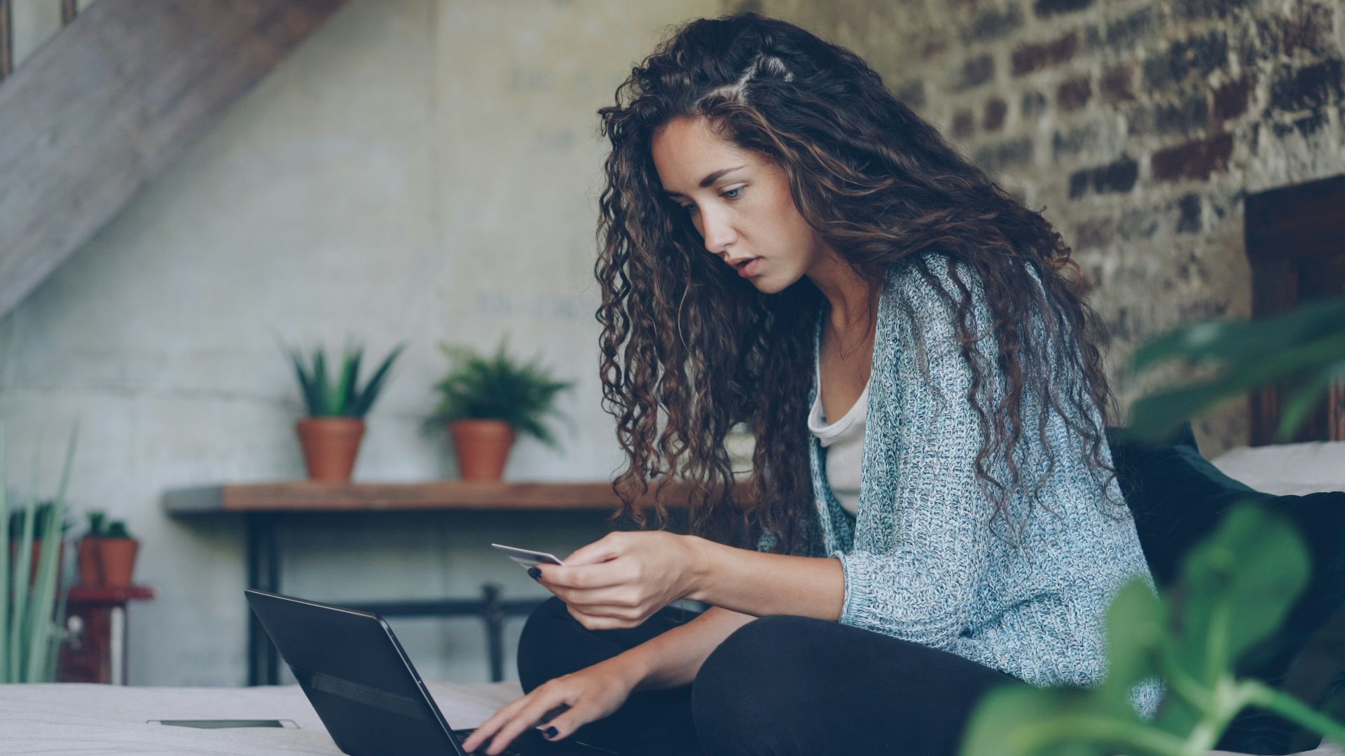 Woman using laptop and credit card on bed.