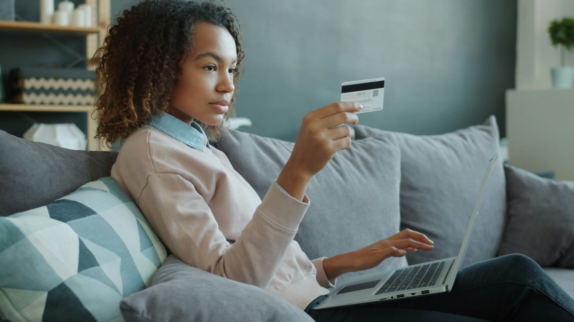 Woman using laptop and credit card on sofa