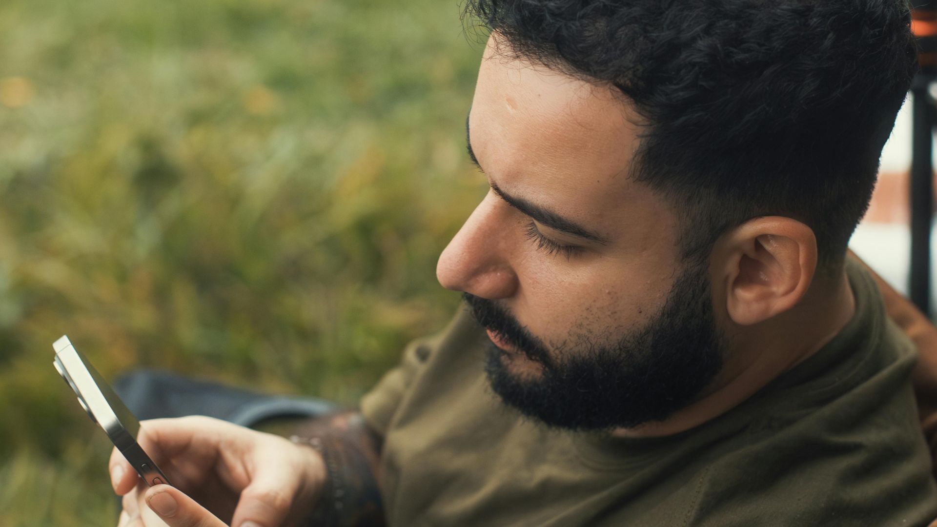 Young man using smartphone while relaxing outdoors, showcasing modern connectivity.