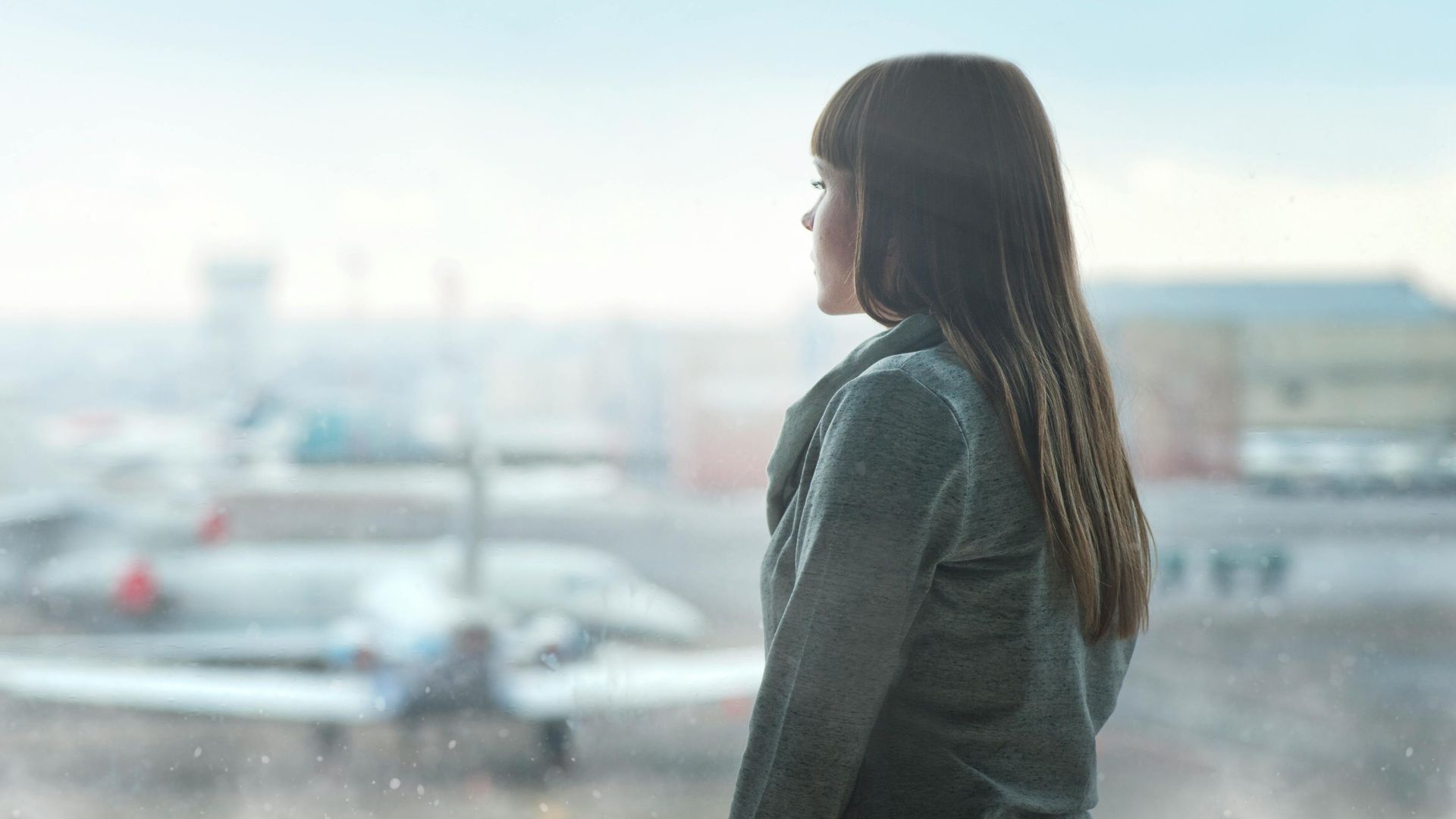 A woman gazing at airplanes through a window at Kyiv's airport terminal, capturing a moment of reflection.