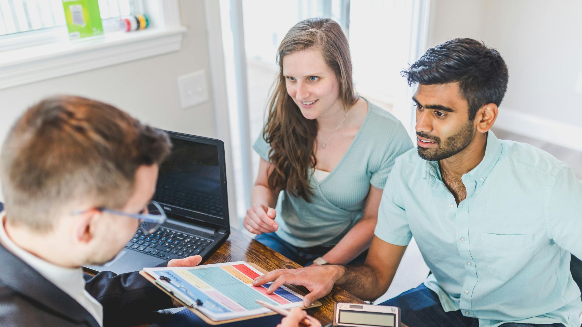 A couple consults with a real estate agent about buying a new home, papers and calculator on the table.