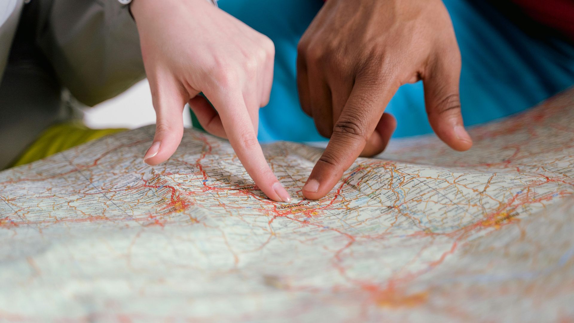 Close-up of diverse hands pointing at a paper map, symbolizing travel planning and navigation.