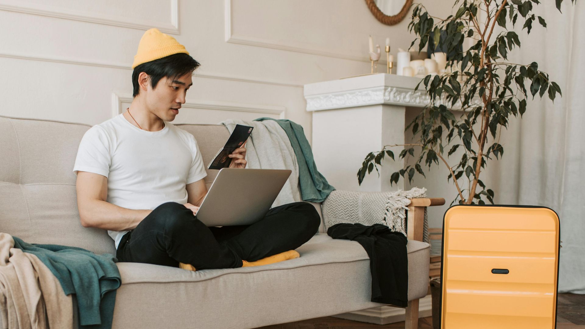 Adult male traveler planning trip at home with laptop and smartphone, surrounded by luggage.