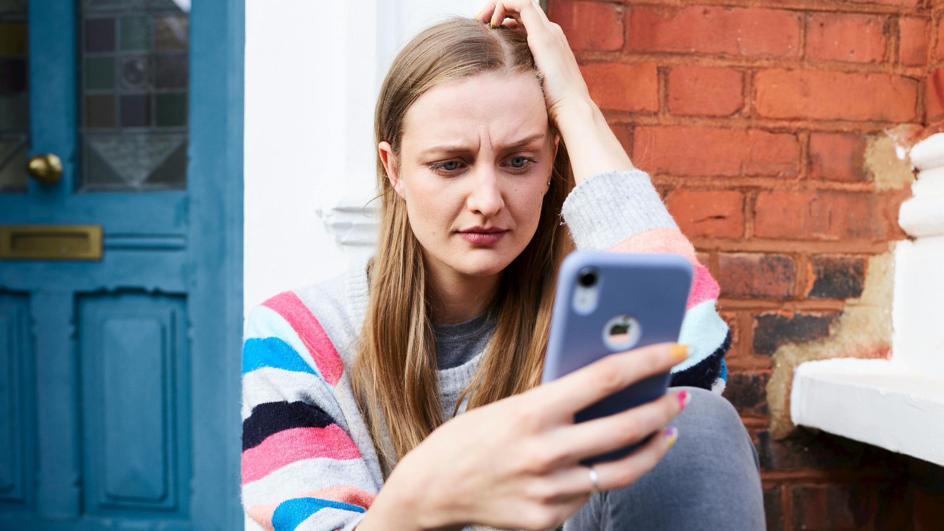 Young woman sitting outside a building, focused on her phone.