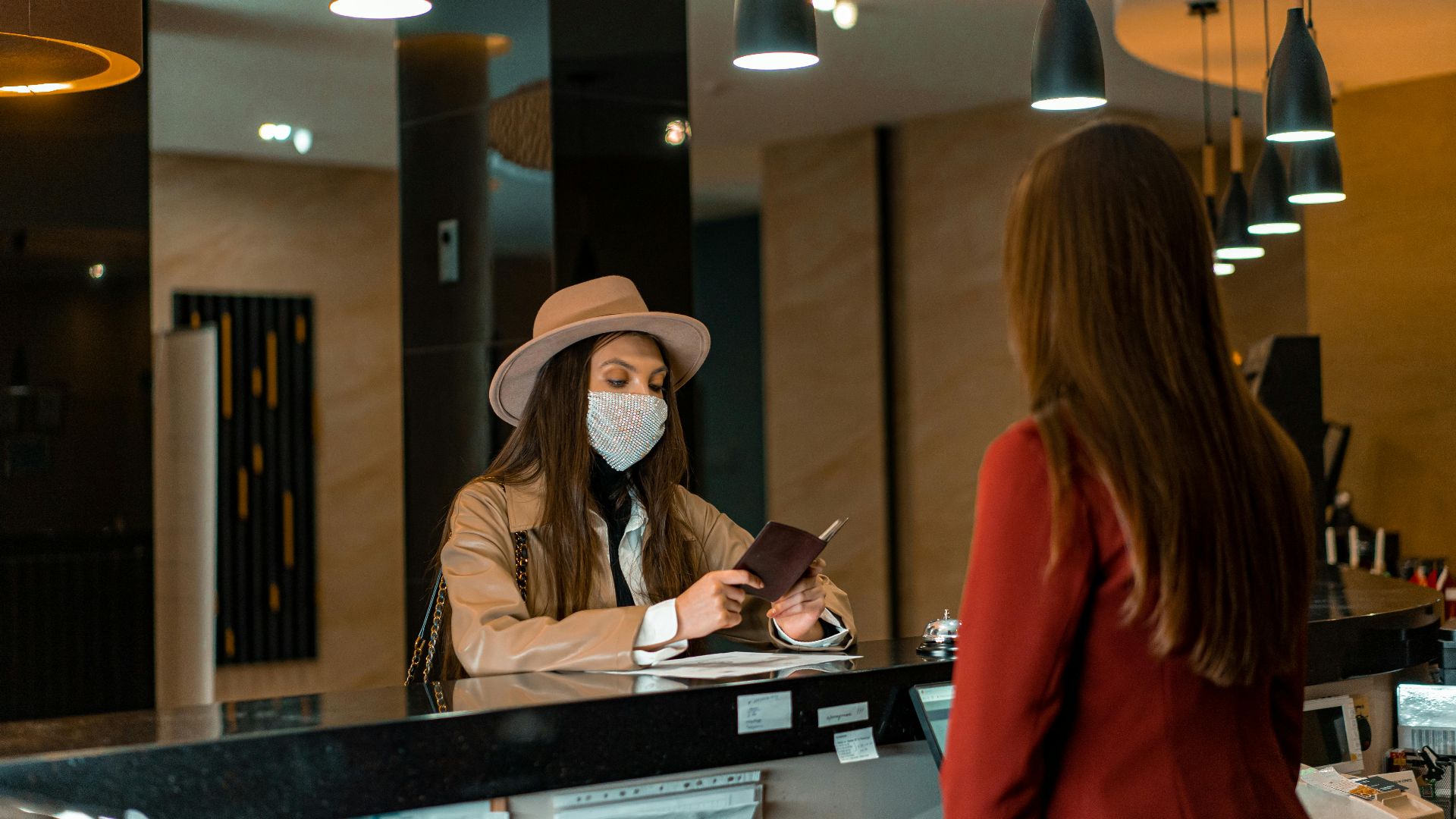 A woman wearing a mask checks in at a hotel reception desk.