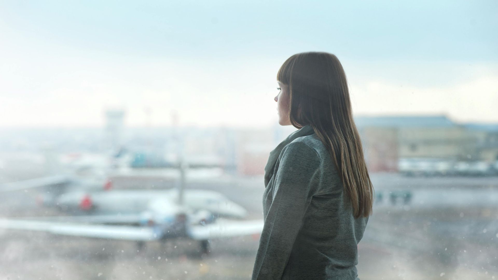 A woman gazing at airplanes through a window at Kyiv's airport terminal, capturing a moment of reflection.