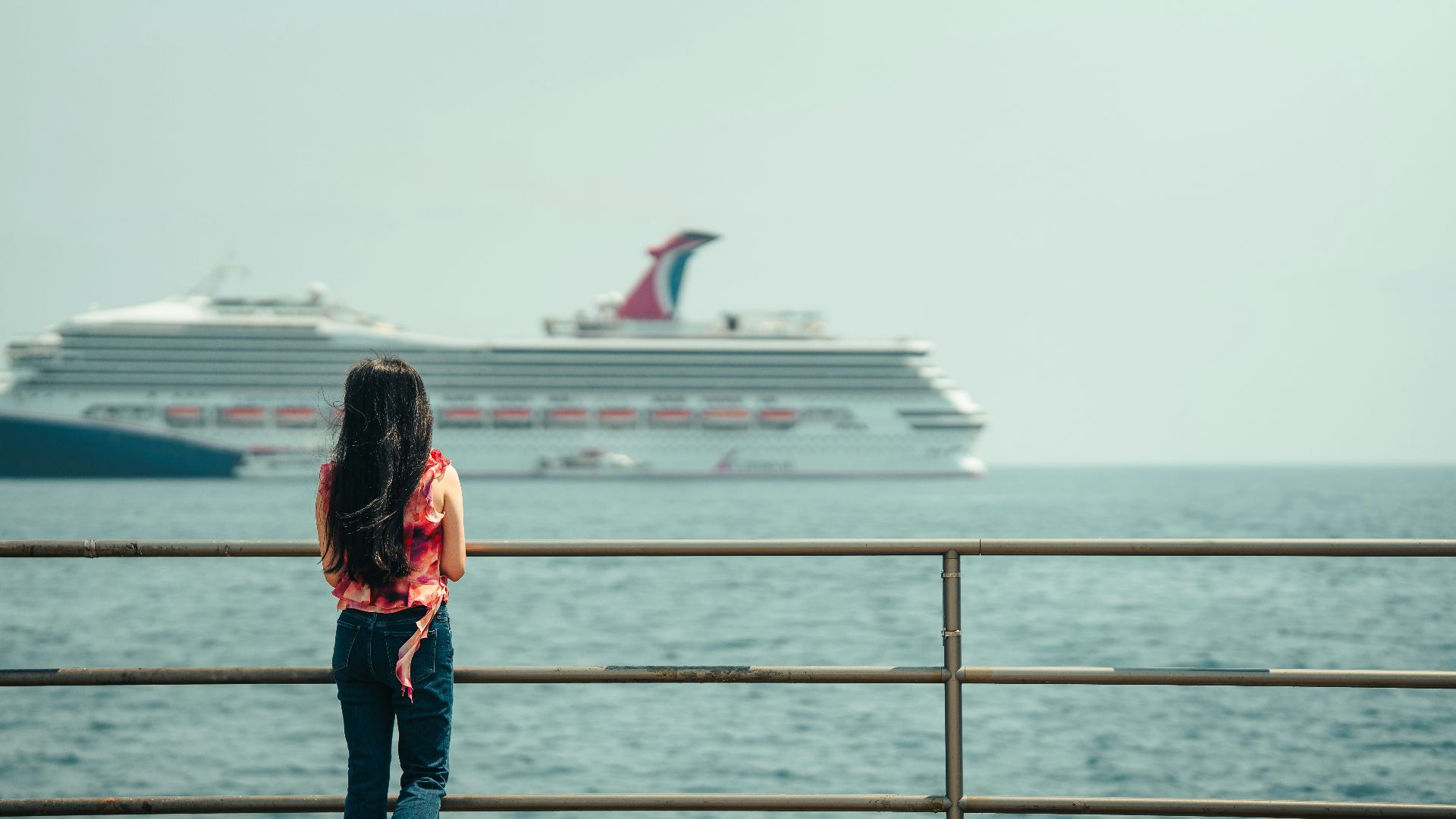 Woman watches a large cruise ship on the ocean.