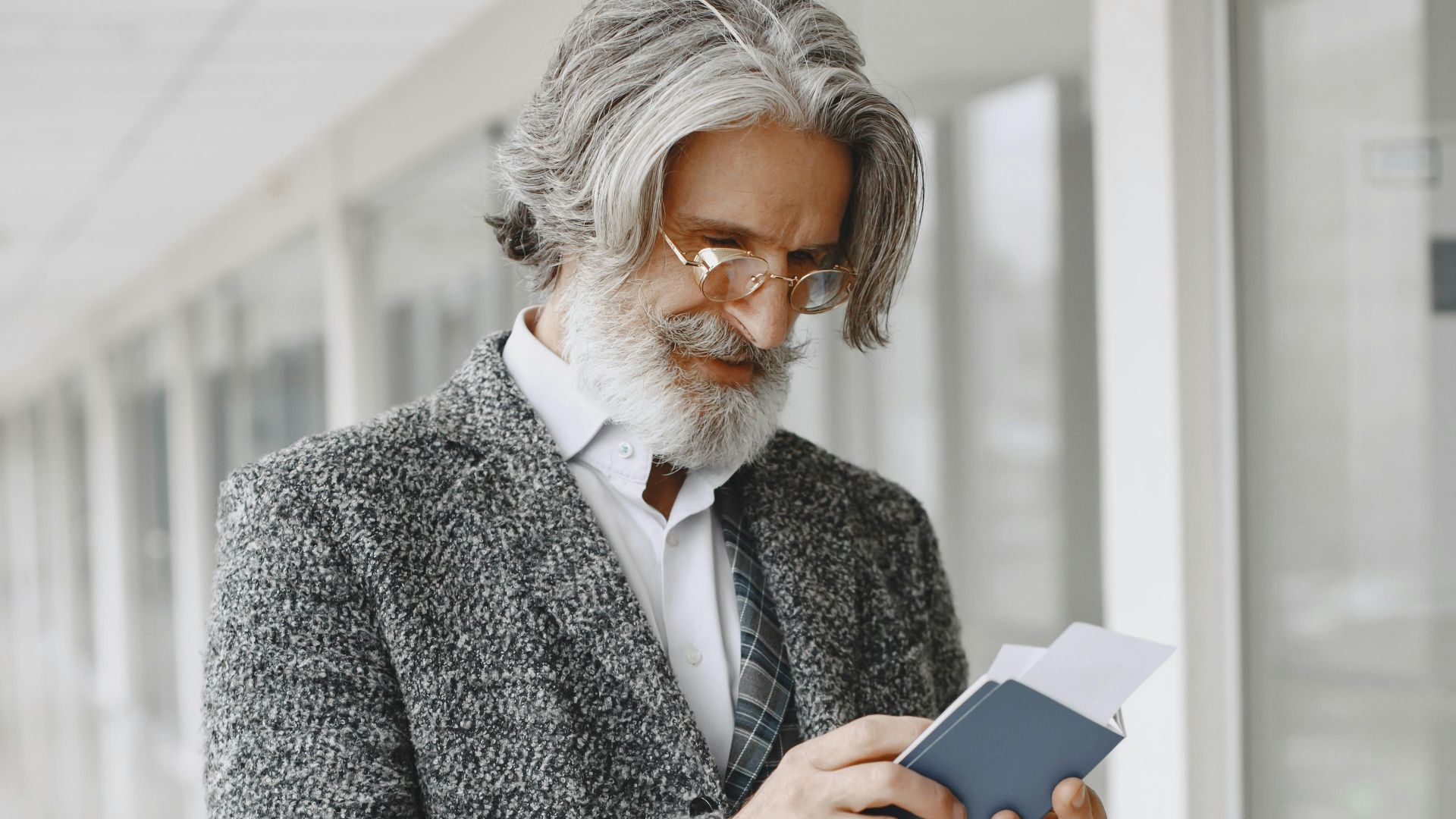 Elegant senior businessman in a suit holding a passport indoors.