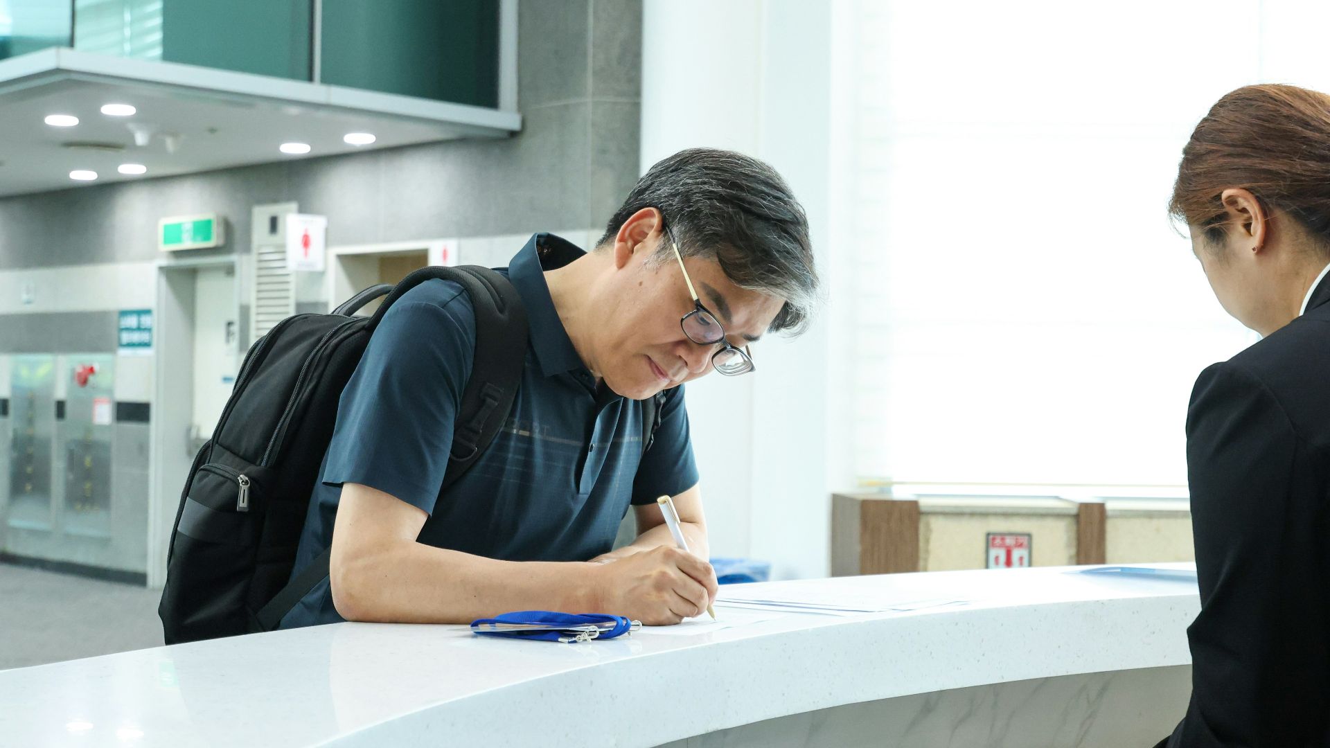A man signs paperwork at a reception desk.