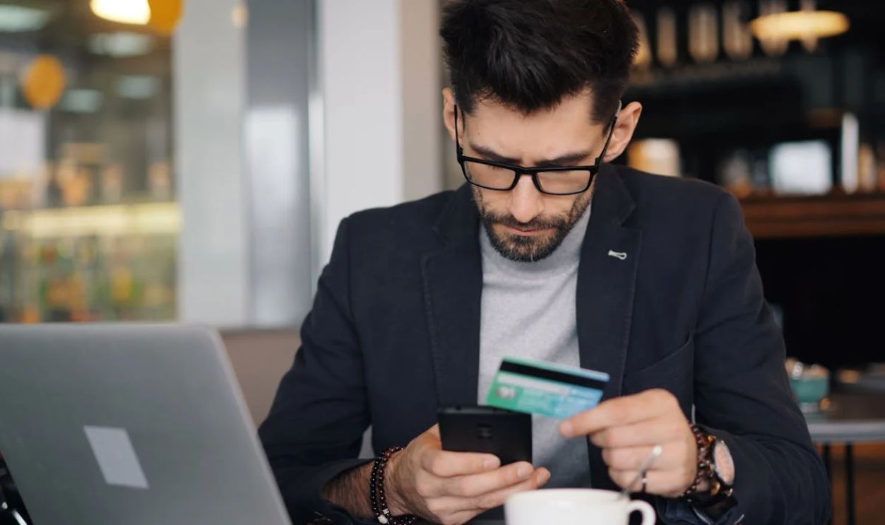 A man in glasses holding a credit card and looking at his phone