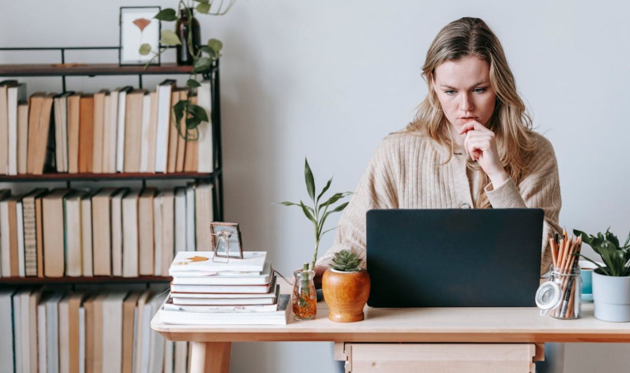 Pensive woman browsing laptop near books