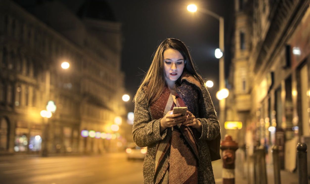 Woman Walking On Sidewalk Holding Smartphone