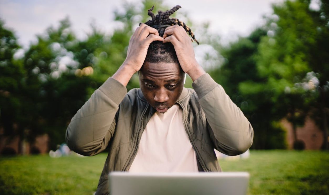 Stressed black male entrepreneur working on laptop in park