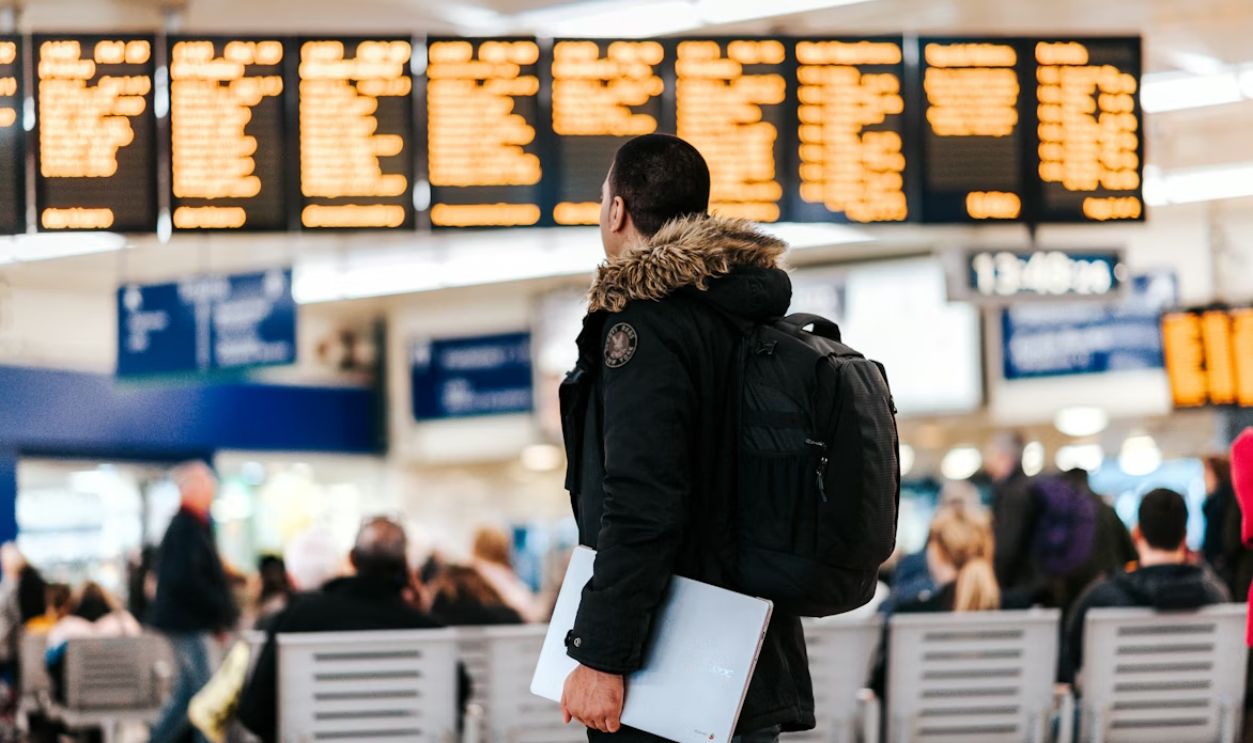 man standing inside airport looking at LED flight schedule bulletin board