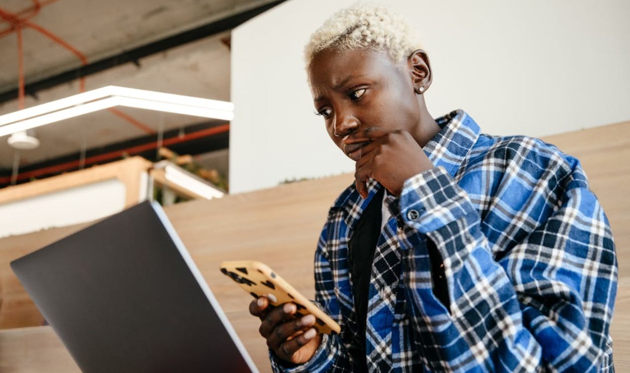 Thoughtful black woman using smartphone and laptop