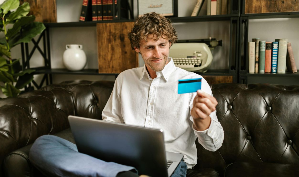 Man in White Dress Shirt Sitting on Black Leather Couch Holding Blue Credit Card