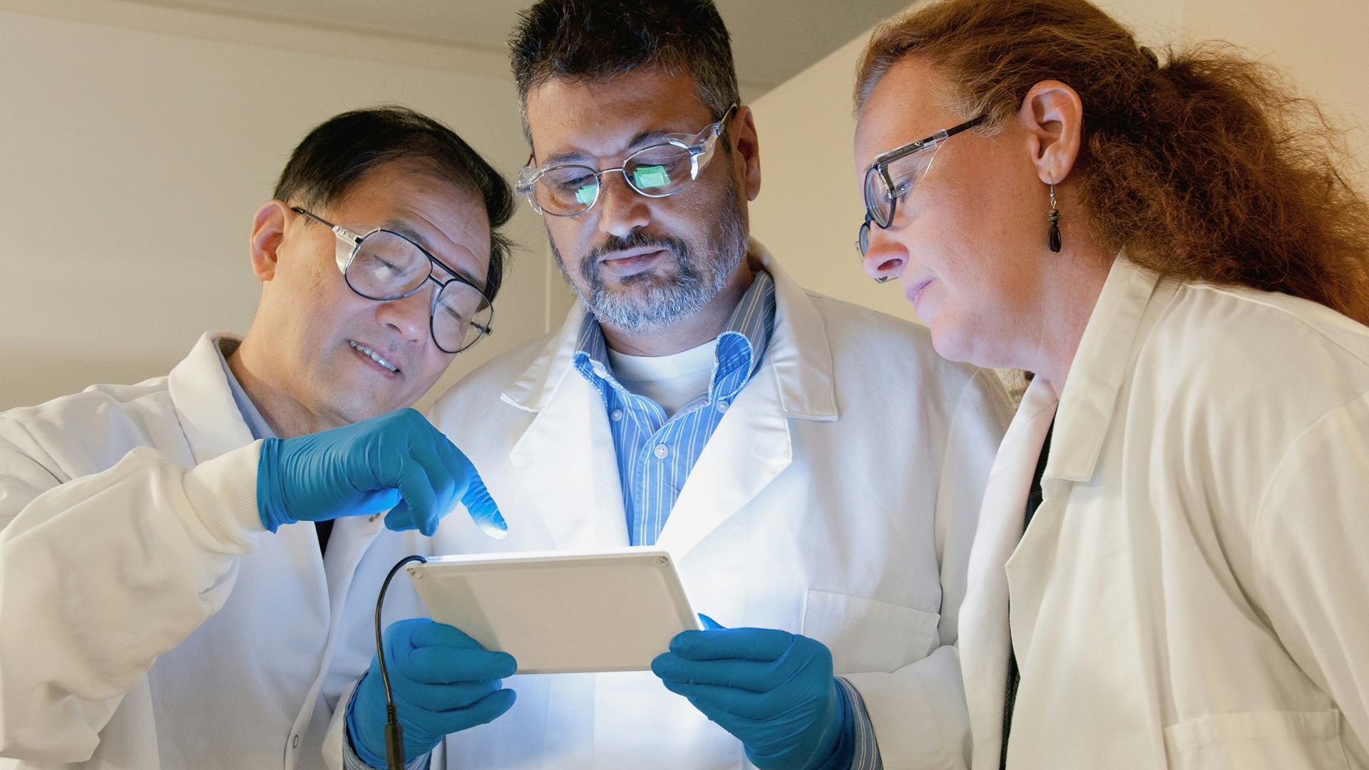 three people in lab coats looking at a tablet