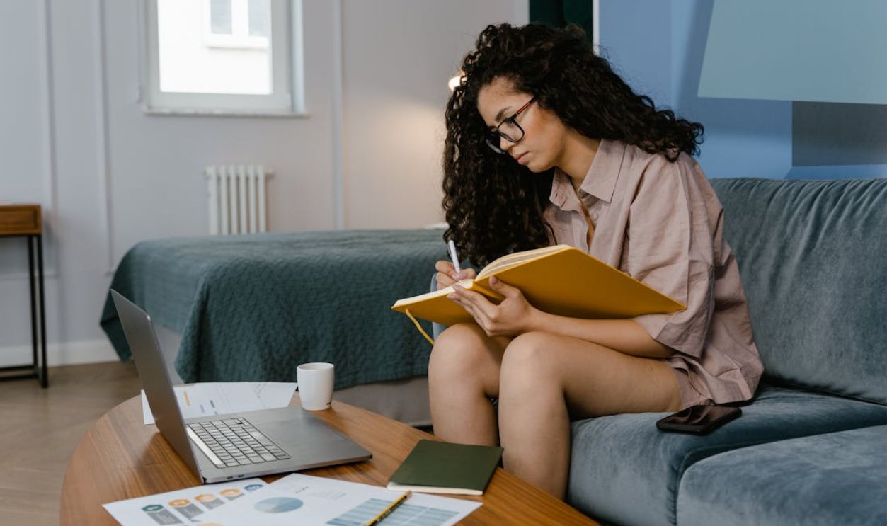A Woman Sitting on Blue Couch Writing on a Notebook