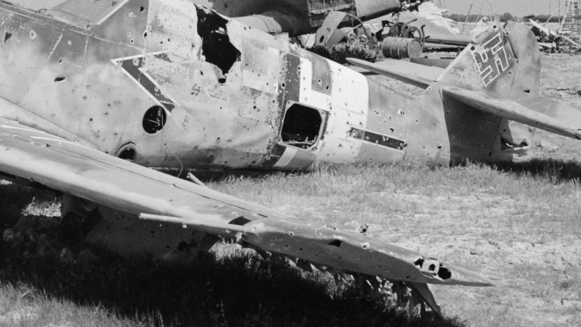 Wreck of German Messerschmitt Bf 109 F/G fighter at El Aouiana airport, Tunis, Tunisia, May 1943. It wears the markings of the adjutant (<) of the 2nd Group (-) of a fighter wing (maybe II./JG 77). Wrecked Junkers Ju 52 transport planes are visible in the background.