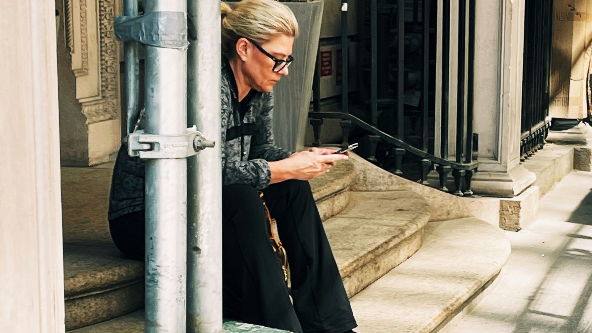 a woman sitting on the steps of a building looking at her cell phone