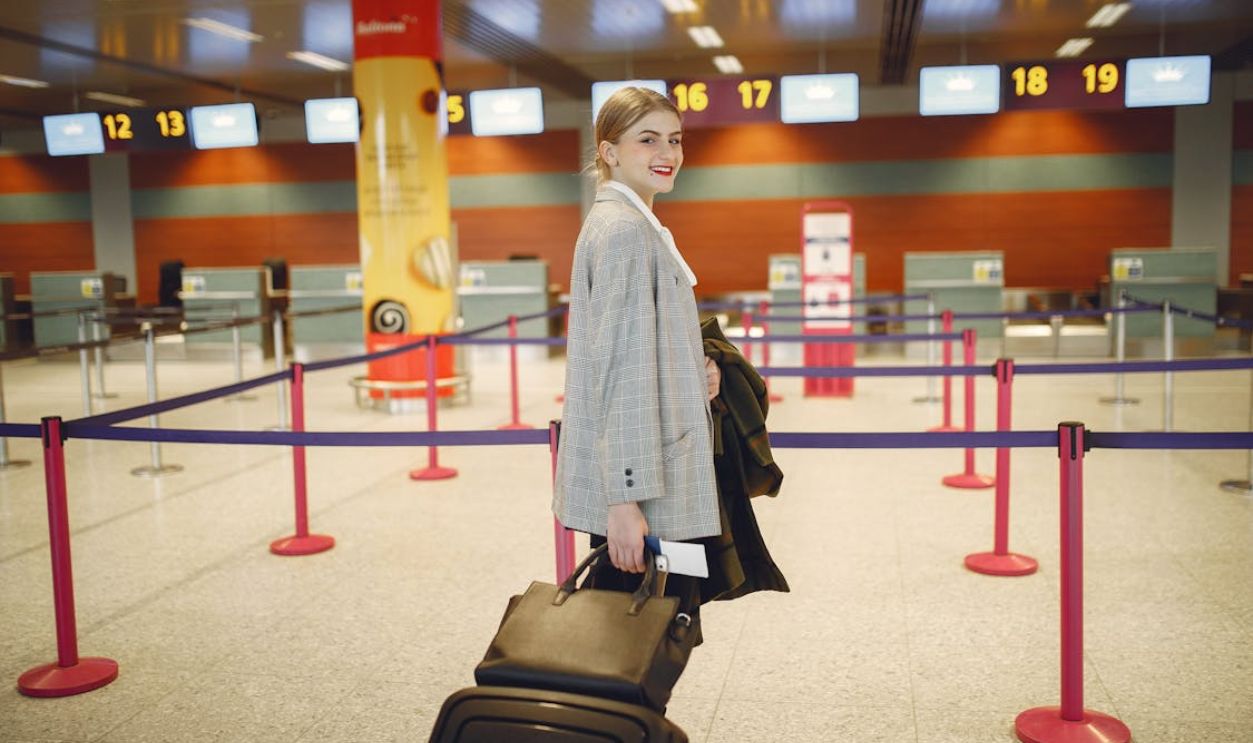Cheerful female passenger walking with luggage to departure check in counter