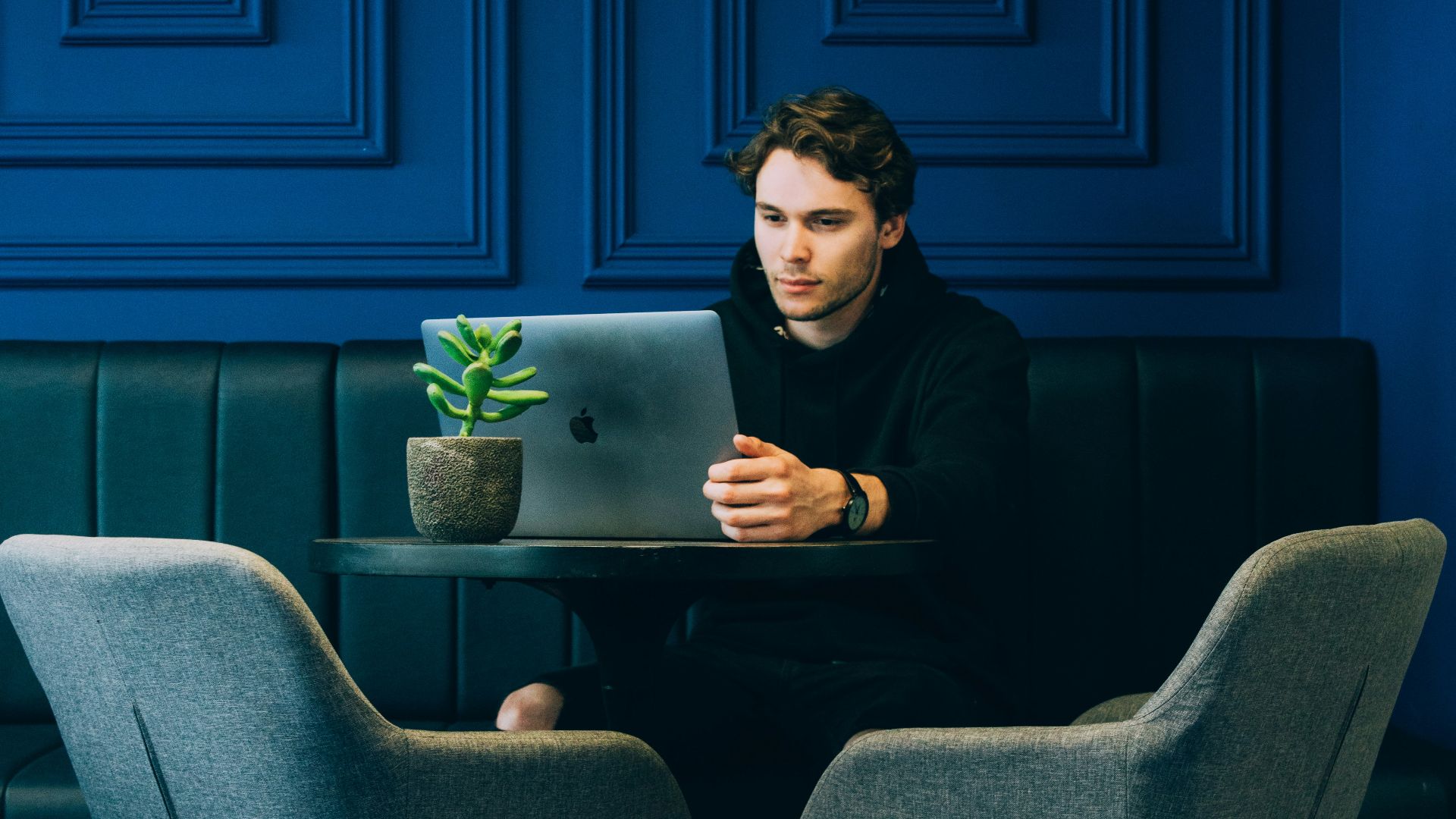 man sitting on couch with looking at his MacBook on table