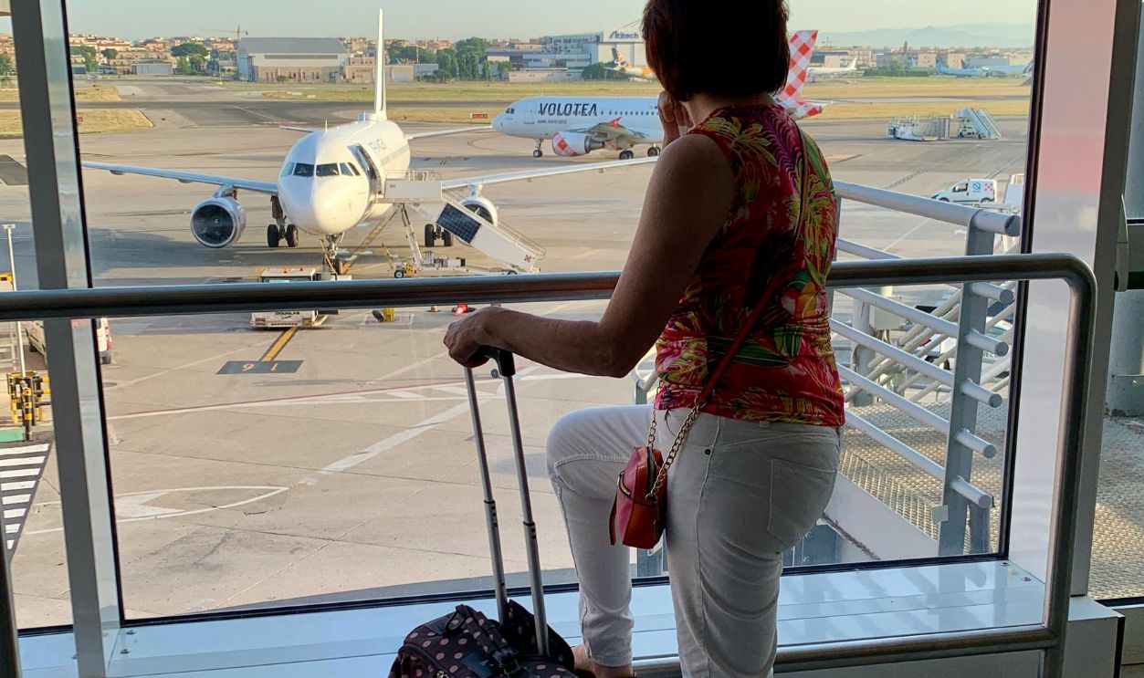 A Woman with Luggage Standing on the Glass Wall Looking at the Parked Airplane on the Tarmac