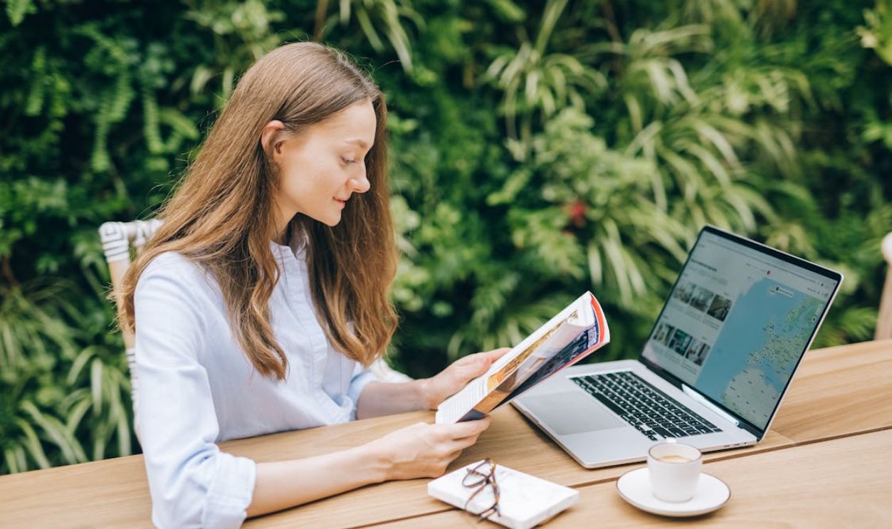 A Smiling Woman Sitting and Reading a Book on a Wood Table