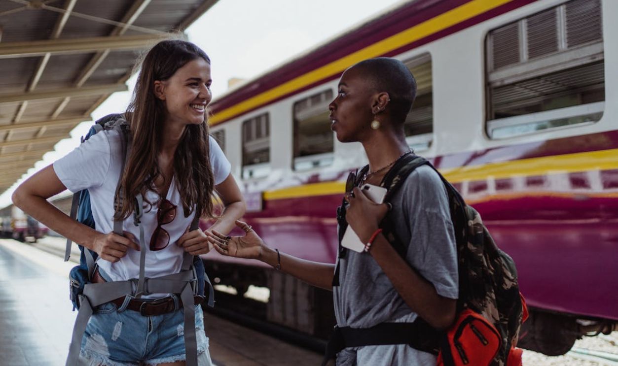 Happy Girls Travelers with Backpacks at Railway Station