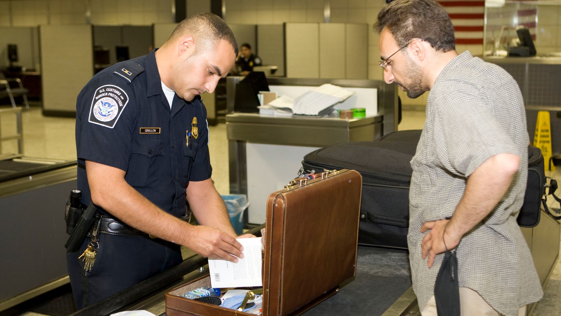 CBP Officer inspects a passengers lugggage at an airport. Photo by James Tourtellotte