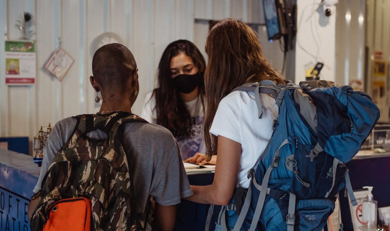 Two Women with Travelling Backpacks Checking In On Reception Desk