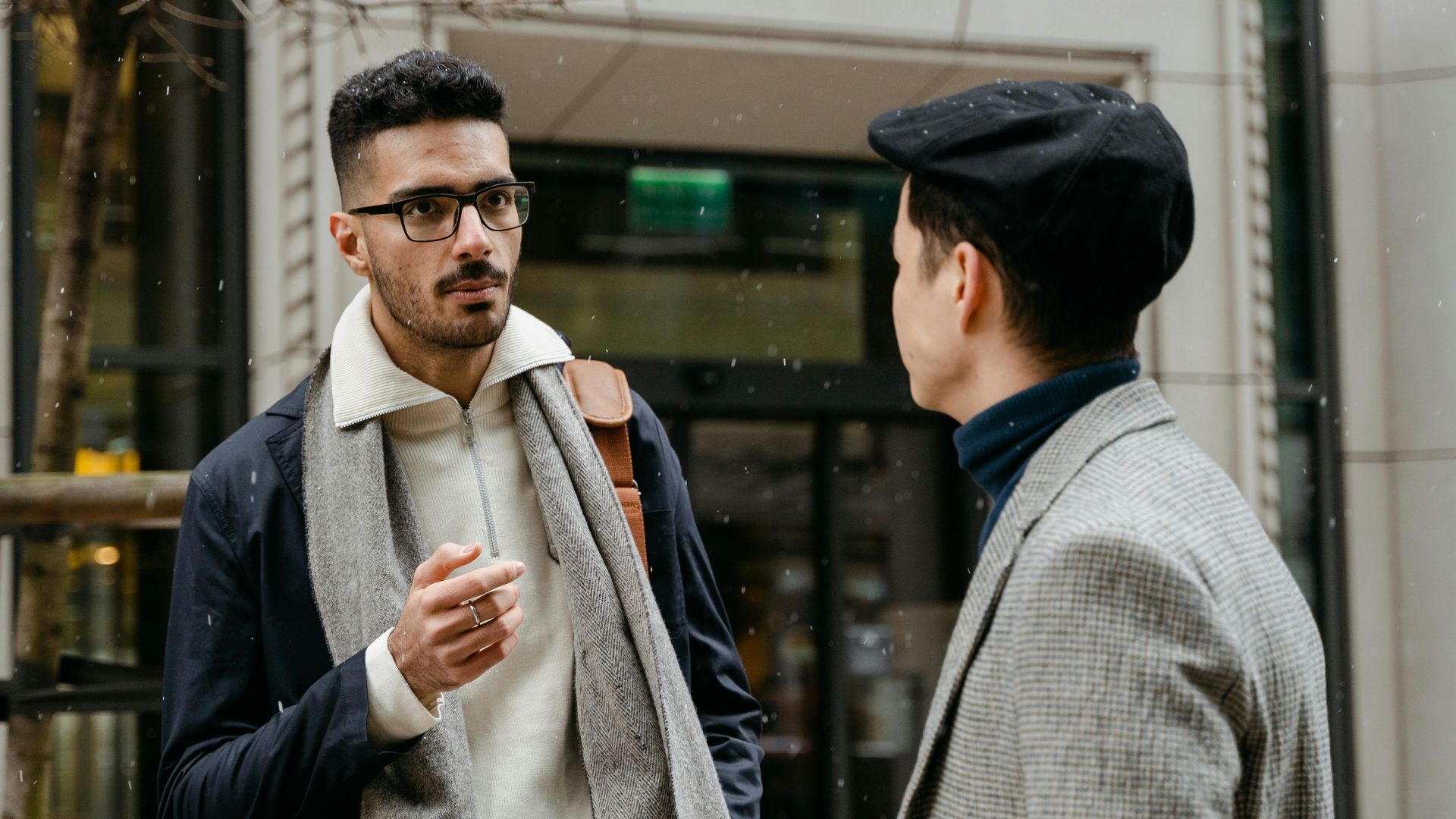 Two businessmen engaged in conversation outside in winter attire with snow falling lightly.