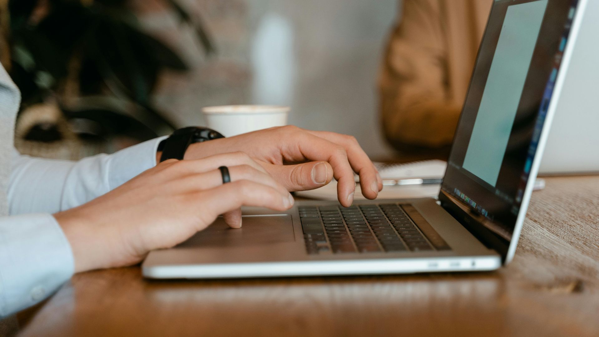 A person typing on a laptop at a wooden table in a modern office setting.