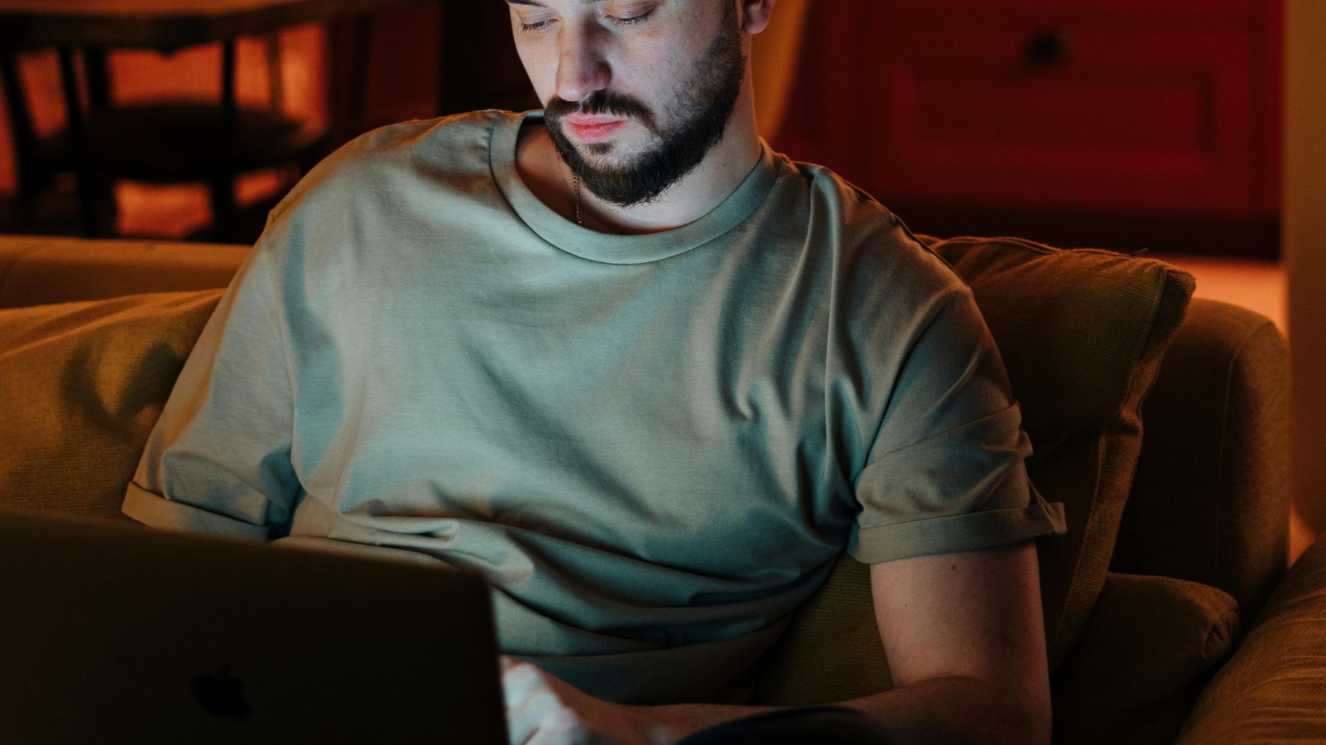 Man working on laptop in cozy home environment with warm lighting.