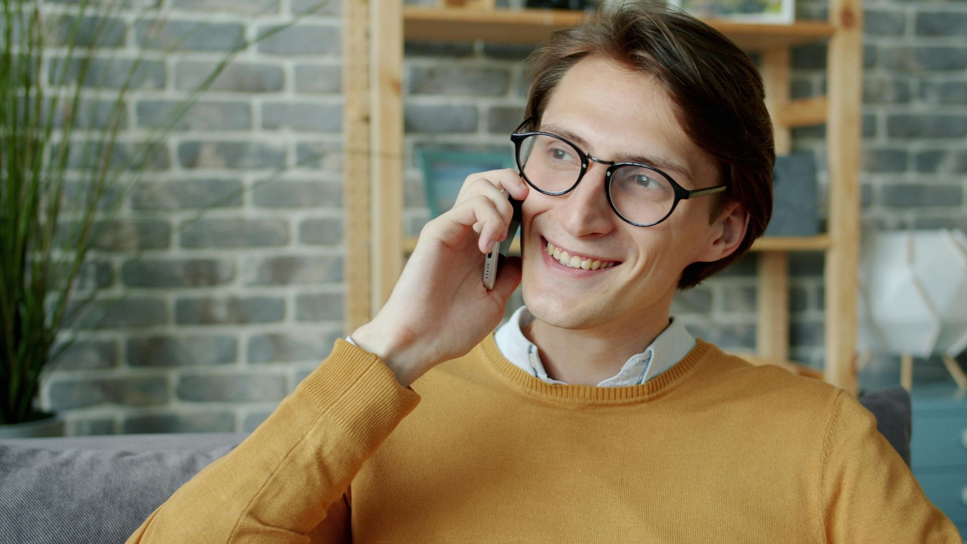 Casually dressed man enjoying a phone call indoors with a smile.