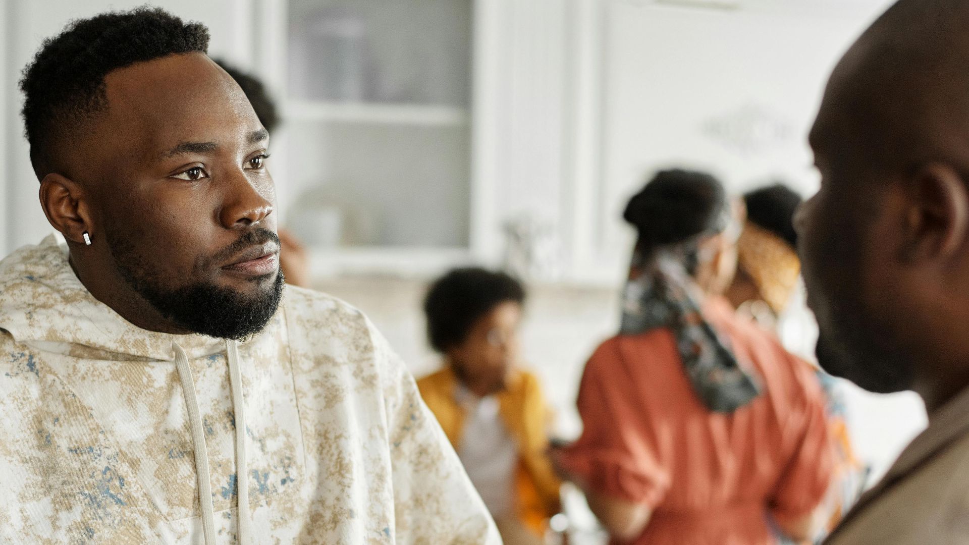 Two friends having a discussion at a casual indoor gathering with others in the background.