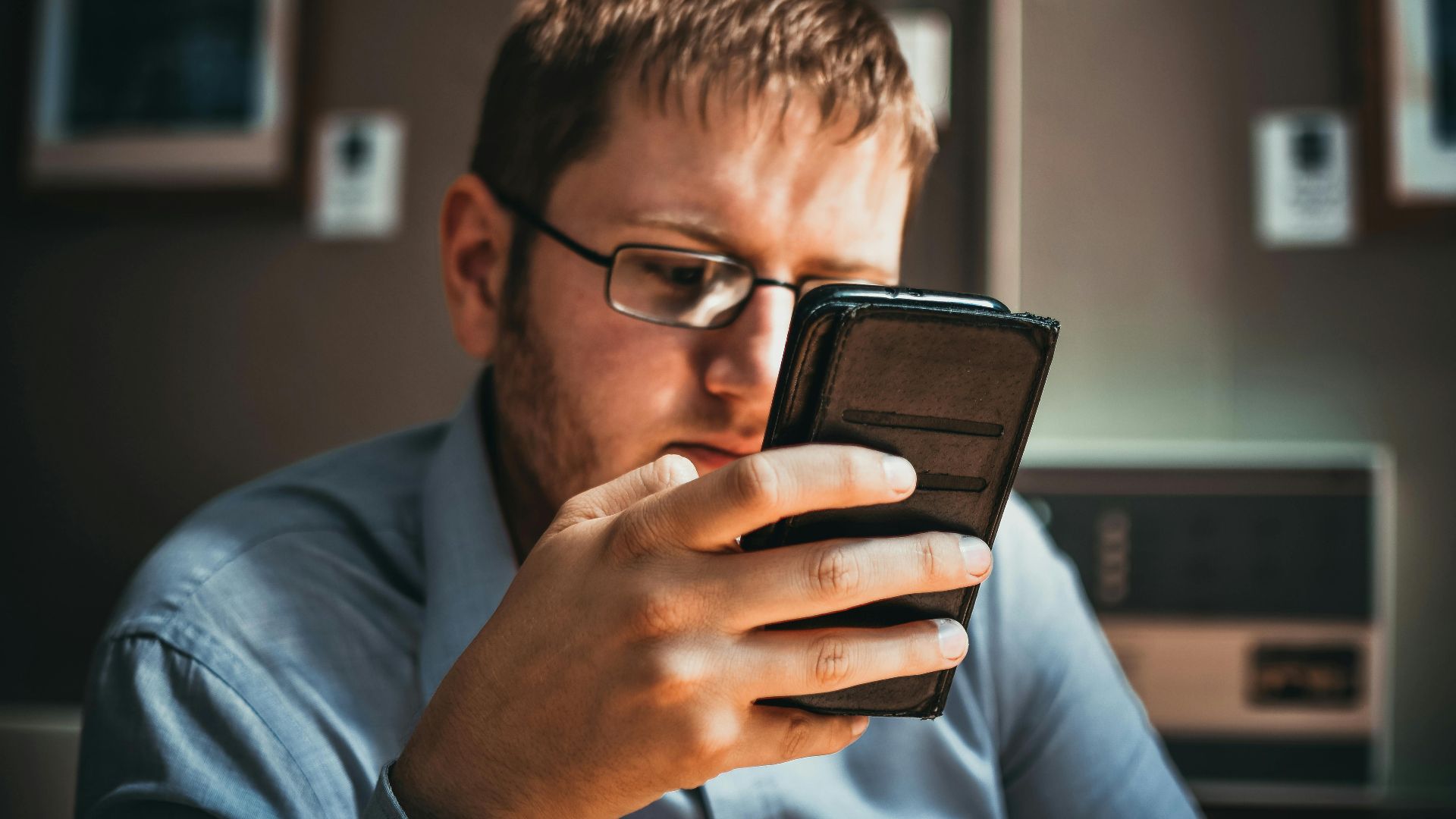 Serious businessman wearing glasses focused on smartphone in a modern office setting.
