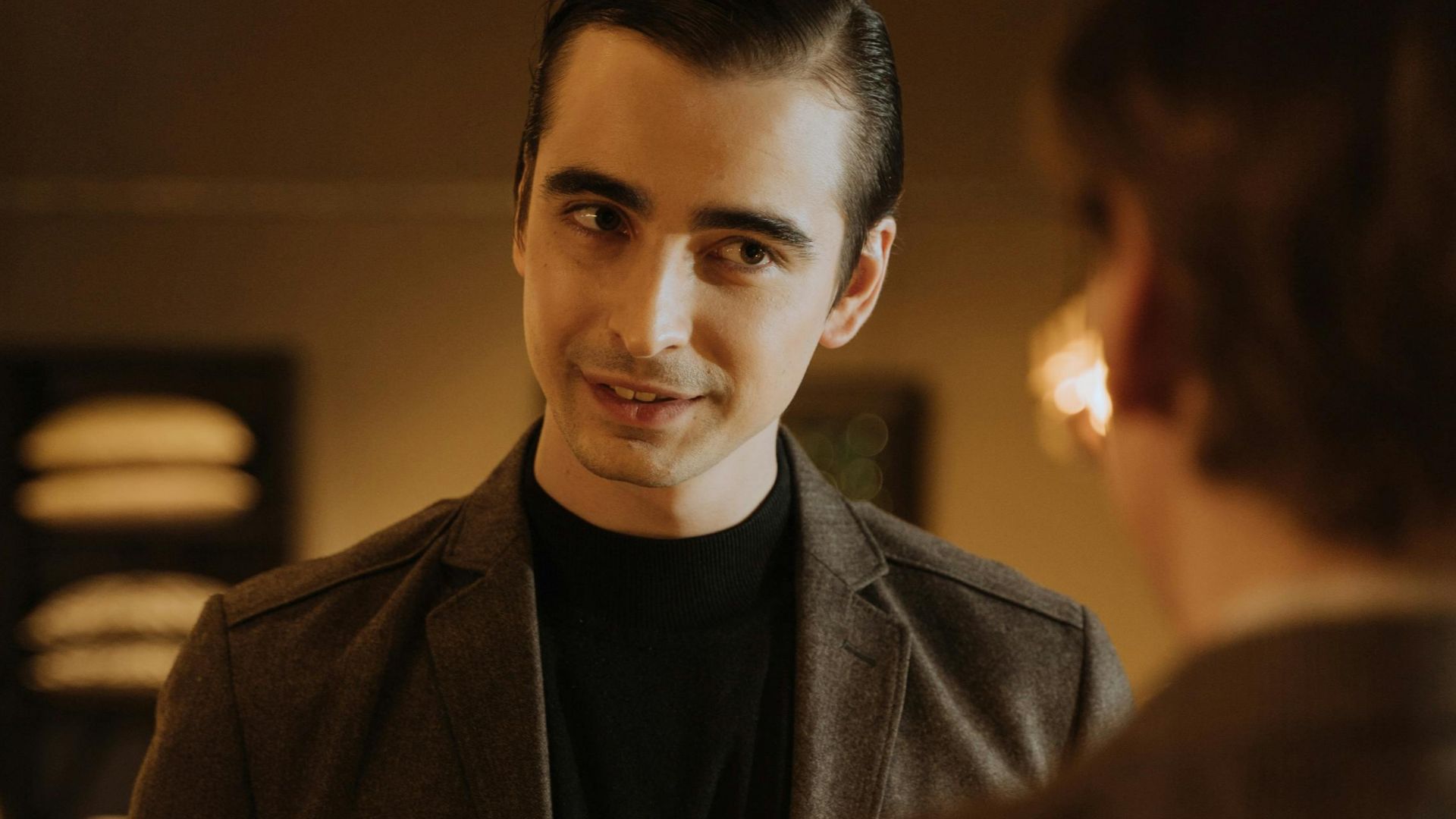 Young adult man in a suit conversing in a warmly lit indoor setting.