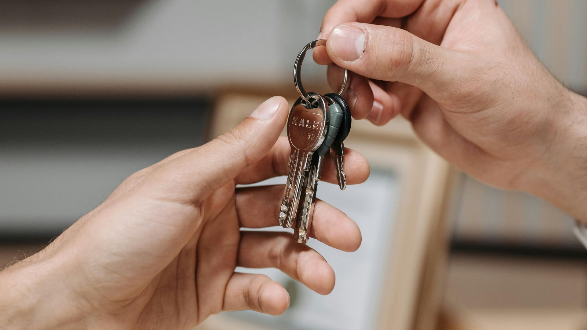 A close-up image of two hands exchanging a set of keys indoors.