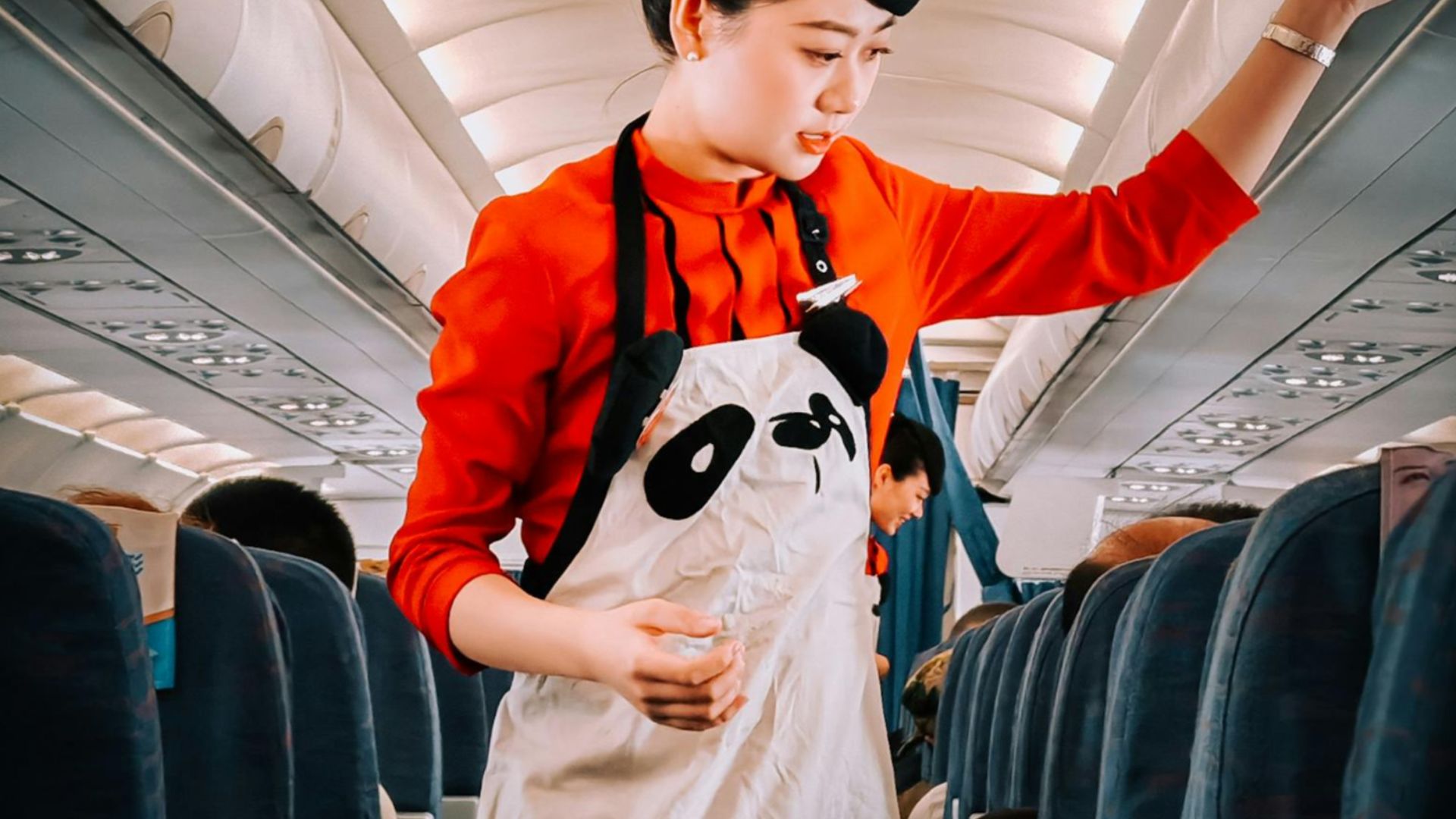 Flight attendant in panda-themed apron assisting passengers during flight.